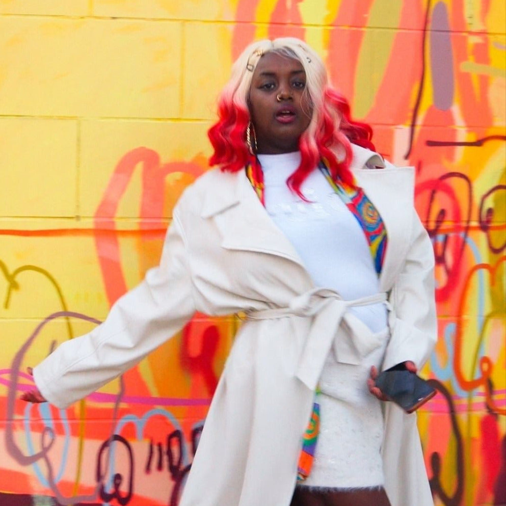 Person with colorful hair standing in front of a graffiti wall with 'Jasmine Kahlia' text.